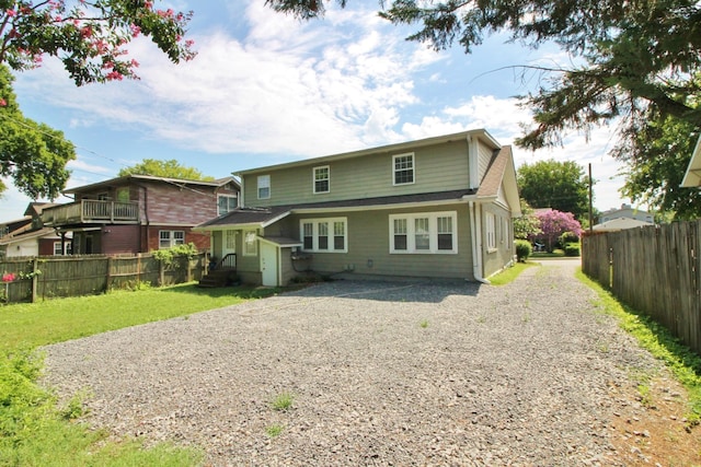 back of property featuring a yard, gravel driveway, and fence