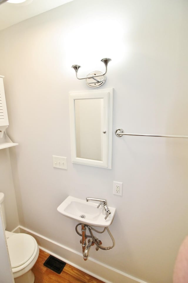 bathroom featuring visible vents, baseboards, toilet, wood finished floors, and a sink