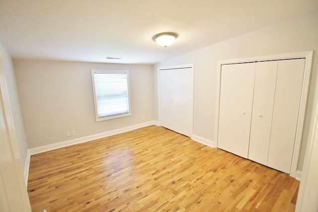 unfurnished bedroom with visible vents, two closets, lofted ceiling, wood finished floors, and baseboards