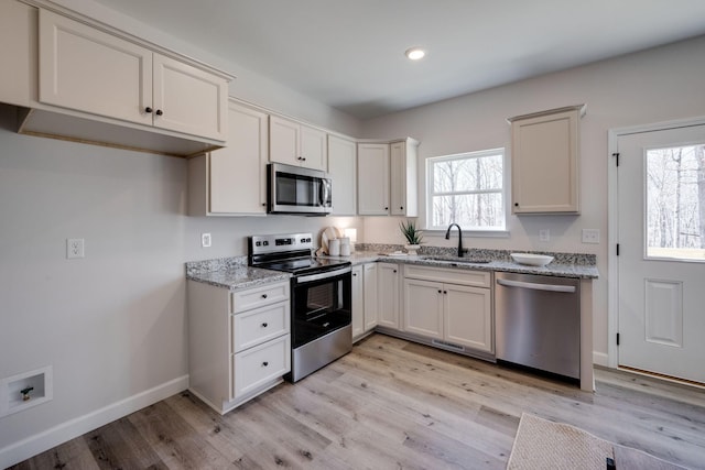 kitchen featuring light stone counters, appliances with stainless steel finishes, light wood-style floors, and a sink