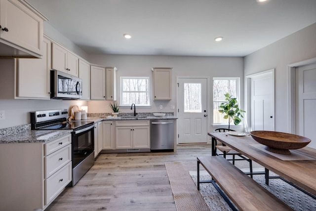 kitchen featuring light stone countertops, recessed lighting, light wood-style flooring, appliances with stainless steel finishes, and a sink