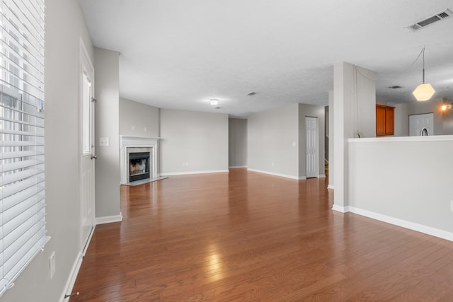 unfurnished living room with wood finished floors, visible vents, and baseboards