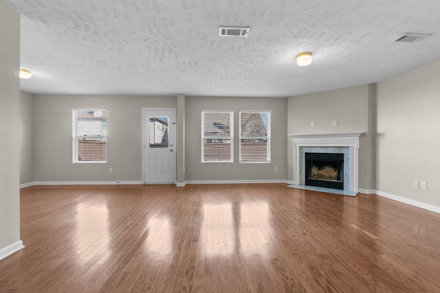 unfurnished living room featuring a high end fireplace, visible vents, baseboards, and wood finished floors