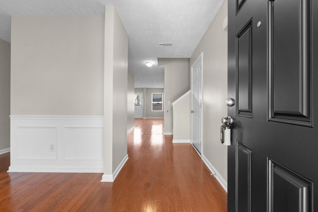 hall featuring baseboards, visible vents, light wood-style flooring, a textured ceiling, and a decorative wall