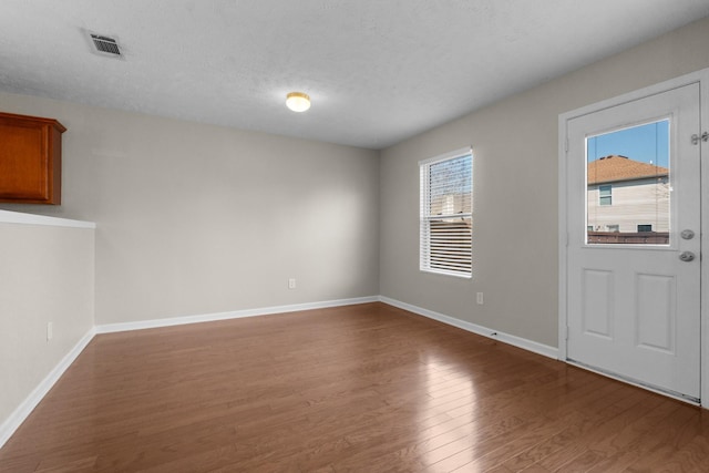 foyer entrance with visible vents, a textured ceiling, baseboards, and wood finished floors