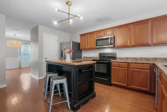 kitchen with a notable chandelier, wood finished floors, brown cabinets, and stainless steel appliances