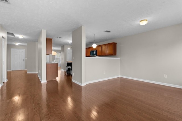 unfurnished living room featuring visible vents, baseboards, a textured ceiling, and dark wood-style floors