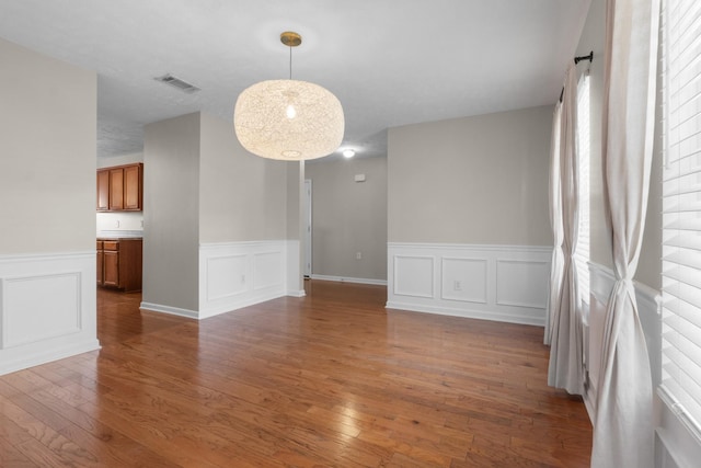 spare room featuring visible vents, wood-type flooring, a wainscoted wall, and a decorative wall