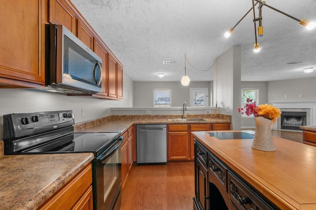 kitchen featuring black appliances, wood finished floors, brown cabinetry, a textured ceiling, and a sink