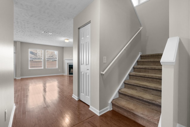 staircase featuring baseboards, wood finished floors, visible vents, and a textured ceiling