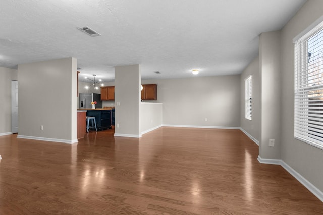 unfurnished living room featuring visible vents, baseboards, a textured ceiling, and dark wood finished floors