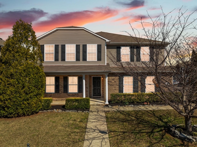 traditional-style house with a porch, a lawn, and brick siding