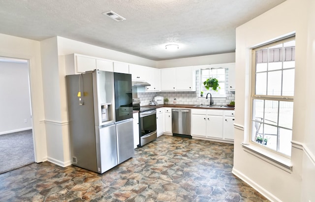 kitchen featuring a sink, under cabinet range hood, appliances with stainless steel finishes, dark countertops, and backsplash