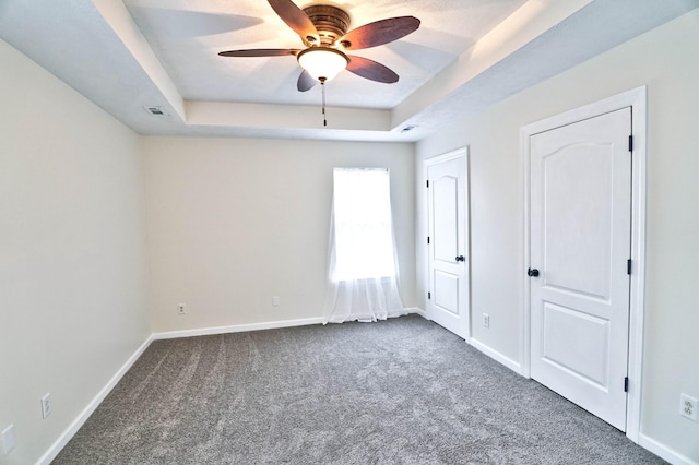 unfurnished bedroom featuring a tray ceiling, baseboards, and carpet floors