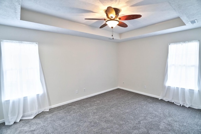 spare room featuring a tray ceiling, carpet, visible vents, and ceiling fan