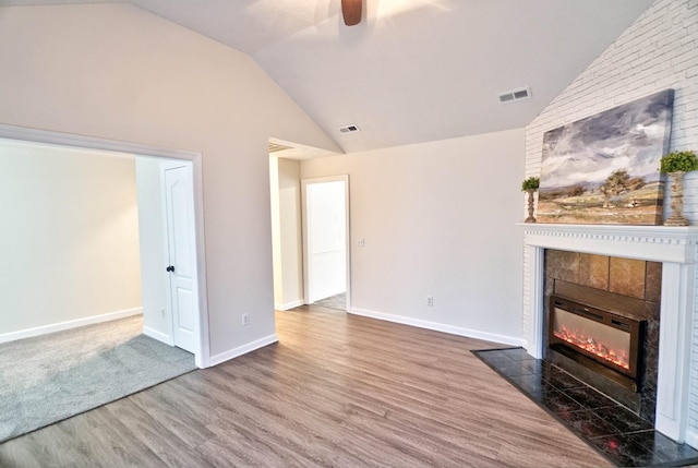 unfurnished living room featuring wood finished floors, a ceiling fan, baseboards, vaulted ceiling, and a tiled fireplace