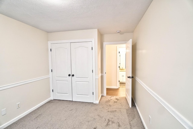 unfurnished bedroom with a textured ceiling, carpet, a closet, and baseboards