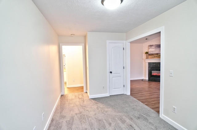 unfurnished bedroom featuring baseboards, a fireplace with flush hearth, a textured ceiling, and carpet flooring