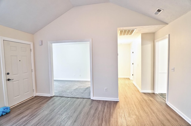 foyer featuring lofted ceiling, wood finished floors, visible vents, and baseboards