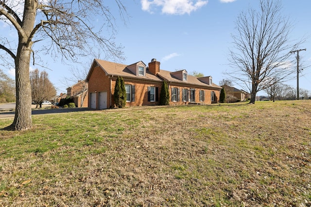 view of front of home featuring driveway, a front yard, a garage, brick siding, and a chimney