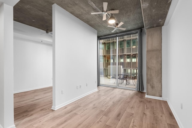 unfurnished room featuring a ceiling fan, a wall of windows, baseboards, and wood finished floors