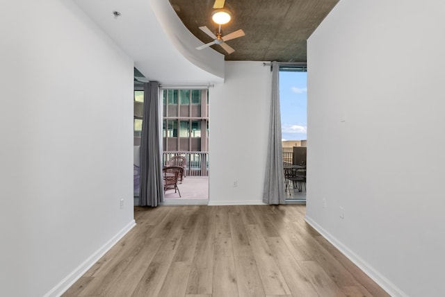 empty room with floor to ceiling windows, a ceiling fan, baseboards, and wood finished floors