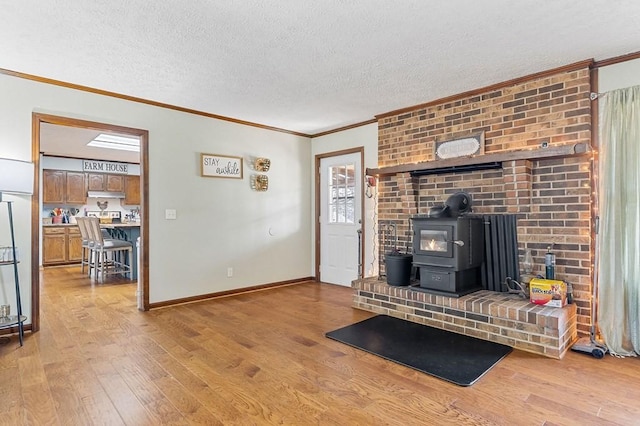 unfurnished living room with light wood-type flooring, a textured ceiling, crown molding, baseboards, and a wood stove