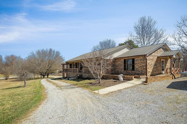 view of side of property featuring brick siding, covered porch, metal roof, a yard, and driveway