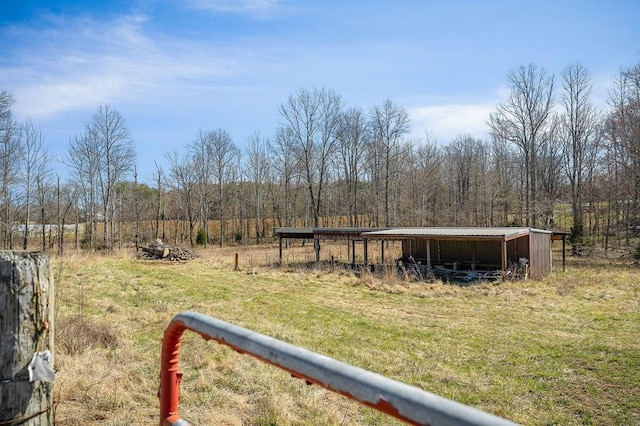 view of yard featuring a rural view, an outdoor structure, an outbuilding, and a view of trees