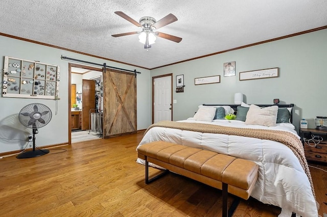 bedroom with a barn door, baseboards, a textured ceiling, and light wood finished floors