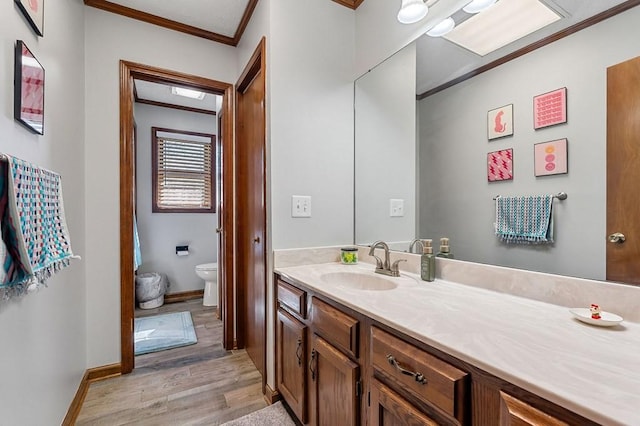 bathroom with toilet, wood finished floors, crown molding, baseboards, and vanity