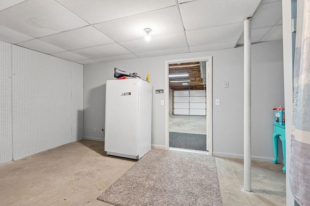 finished below grade area with baseboards, a paneled ceiling, and freestanding refrigerator