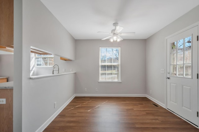 unfurnished dining area with visible vents, baseboards, wood finished floors, a ceiling fan, and a sink