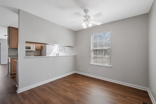 interior space featuring a ceiling fan, visible vents, dark wood-style floors, and baseboards