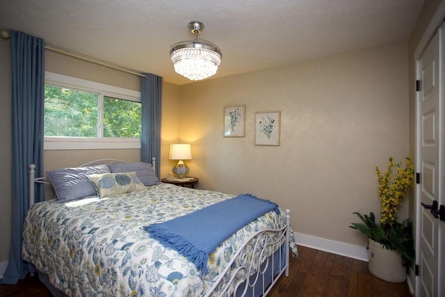 bedroom featuring a notable chandelier, a textured ceiling, baseboards, and wood finished floors