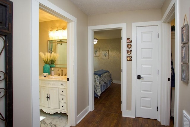 hall featuring a sink, baseboards, dark wood-type flooring, and a textured ceiling