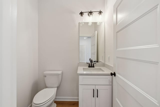 half bath featuring baseboards, toilet, wood finished floors, and vanity