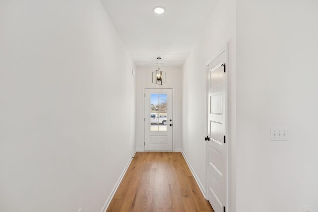 entryway with an inviting chandelier, baseboards, and light wood-type flooring
