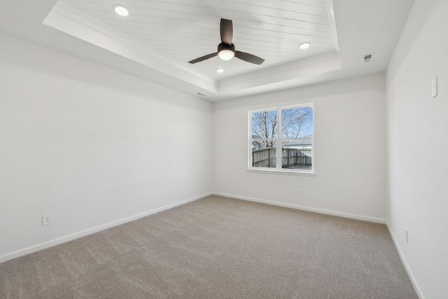 empty room with visible vents, a raised ceiling, baseboards, and carpet flooring
