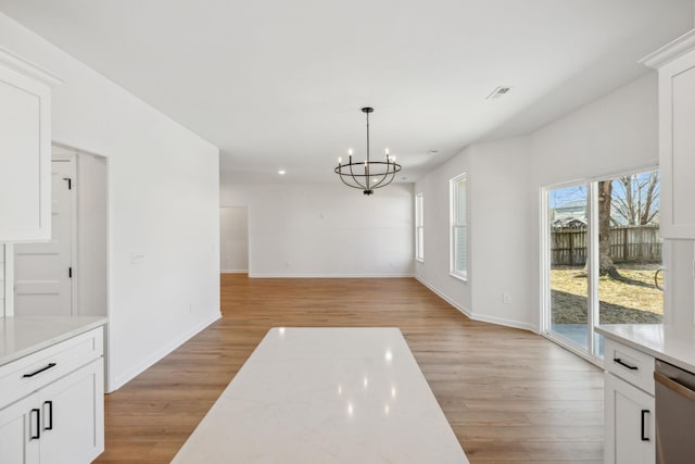 unfurnished dining area featuring baseboards, light wood-style floors, visible vents, and a chandelier