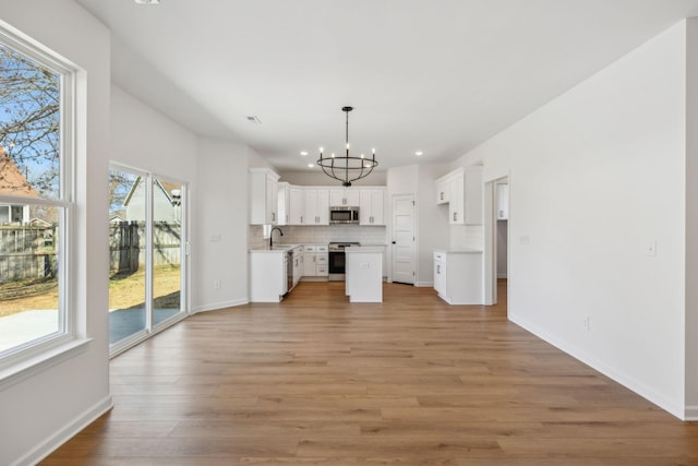 kitchen with light wood-type flooring, a sink, stainless steel appliances, white cabinets, and decorative backsplash