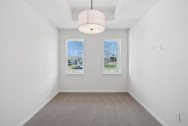 carpeted empty room featuring baseboards and a raised ceiling
