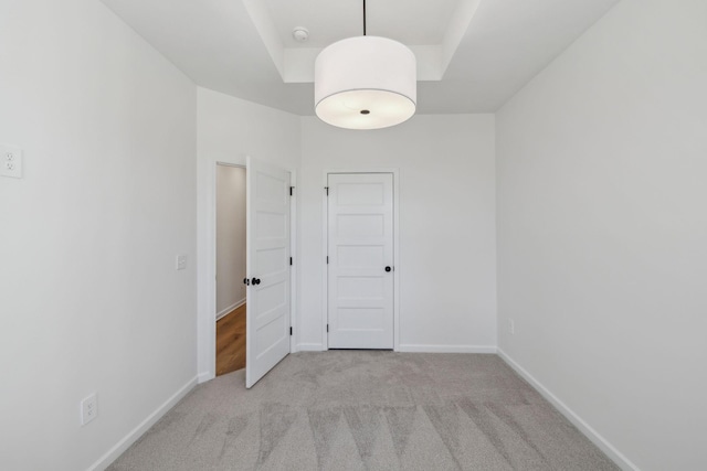 carpeted spare room featuring a tray ceiling and baseboards
