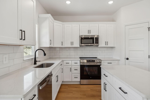 kitchen with light wood finished floors, a sink, decorative backsplash, stainless steel appliances, and white cabinets