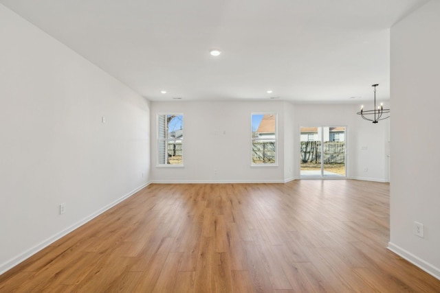unfurnished living room featuring baseboards, plenty of natural light, light wood-style floors, and a chandelier