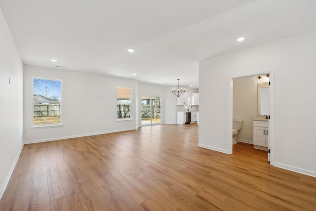 unfurnished living room featuring a notable chandelier, recessed lighting, light wood-type flooring, and baseboards