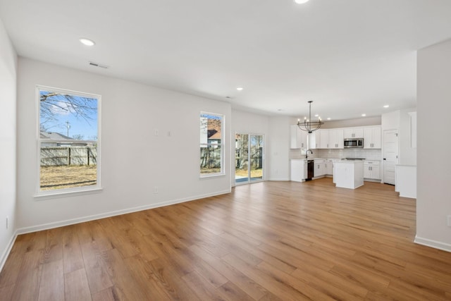 unfurnished living room featuring light wood-type flooring, visible vents, a healthy amount of sunlight, and an inviting chandelier
