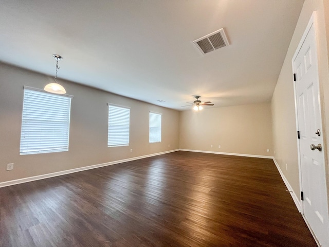 spare room with a ceiling fan, visible vents, dark wood-style flooring, and baseboards