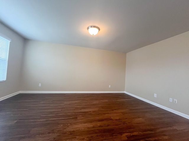 spare room featuring baseboards and dark wood-style flooring