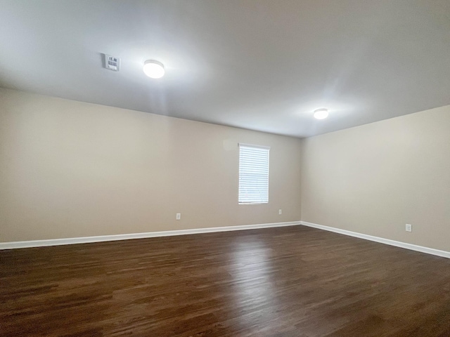 unfurnished room with dark wood finished floors, visible vents, and baseboards